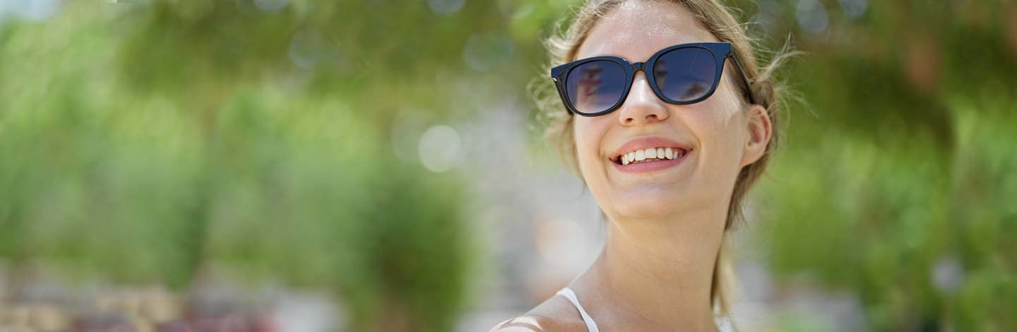 Young blonde woman wearing sunglasses looking to the sky smiling at park