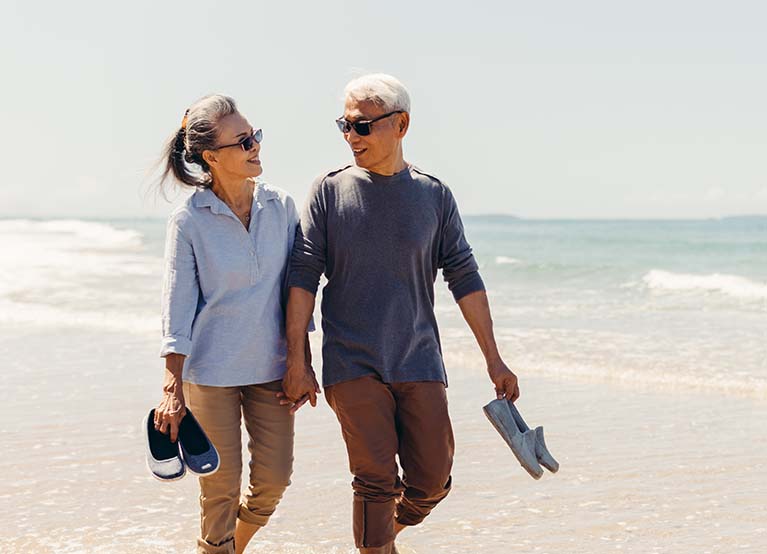 Romantic Senior couple strolling happily along the beach in the sunshine and bright sky. Retirement concept and happy life.
