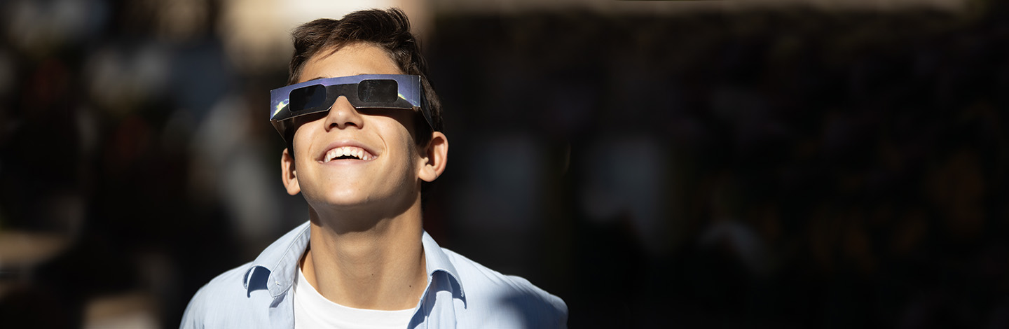 teenager smiling and looking at the eclipse with eclipse safety glasses on.jpg